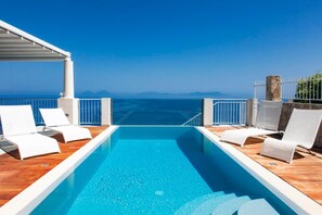 A pool area with white lounge chairs and a view of the sea.