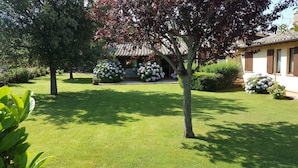 Een goed onderhouden tuin met gazon, diverse struiken en een gebouw met pannendak.