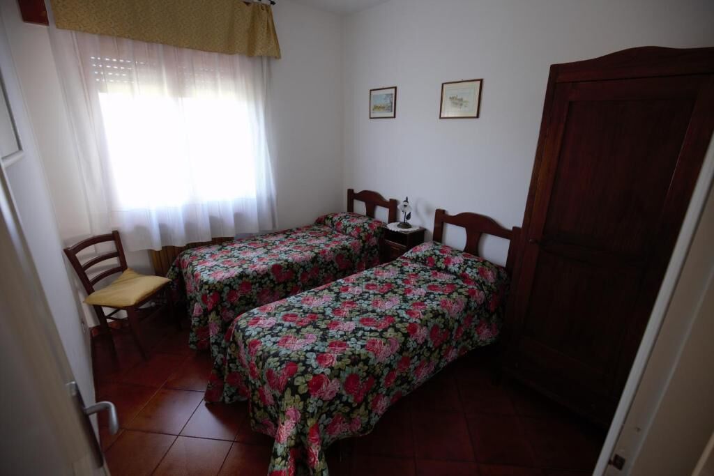 A small bedroom with two single beds, a chair, a small table, and a wooden wardrobe.