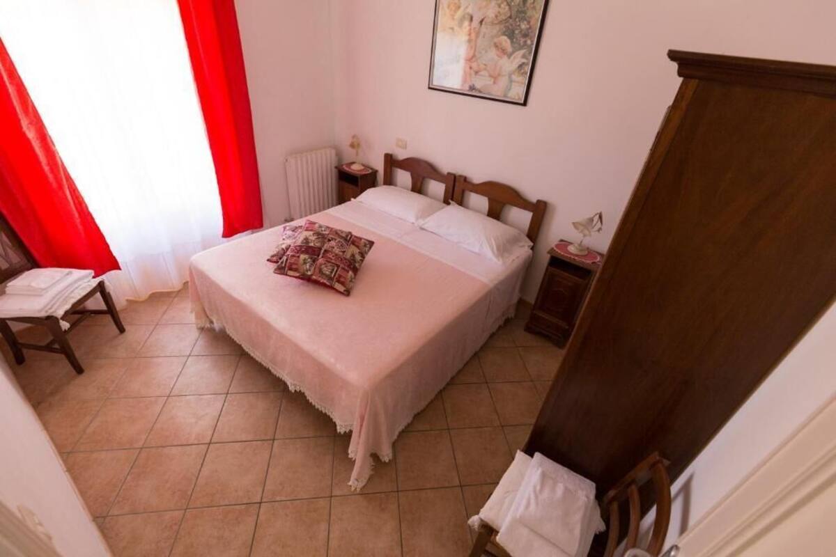 A bedroom with a bed, a nightstand, a chair, a radiator, and a painting on the wall.