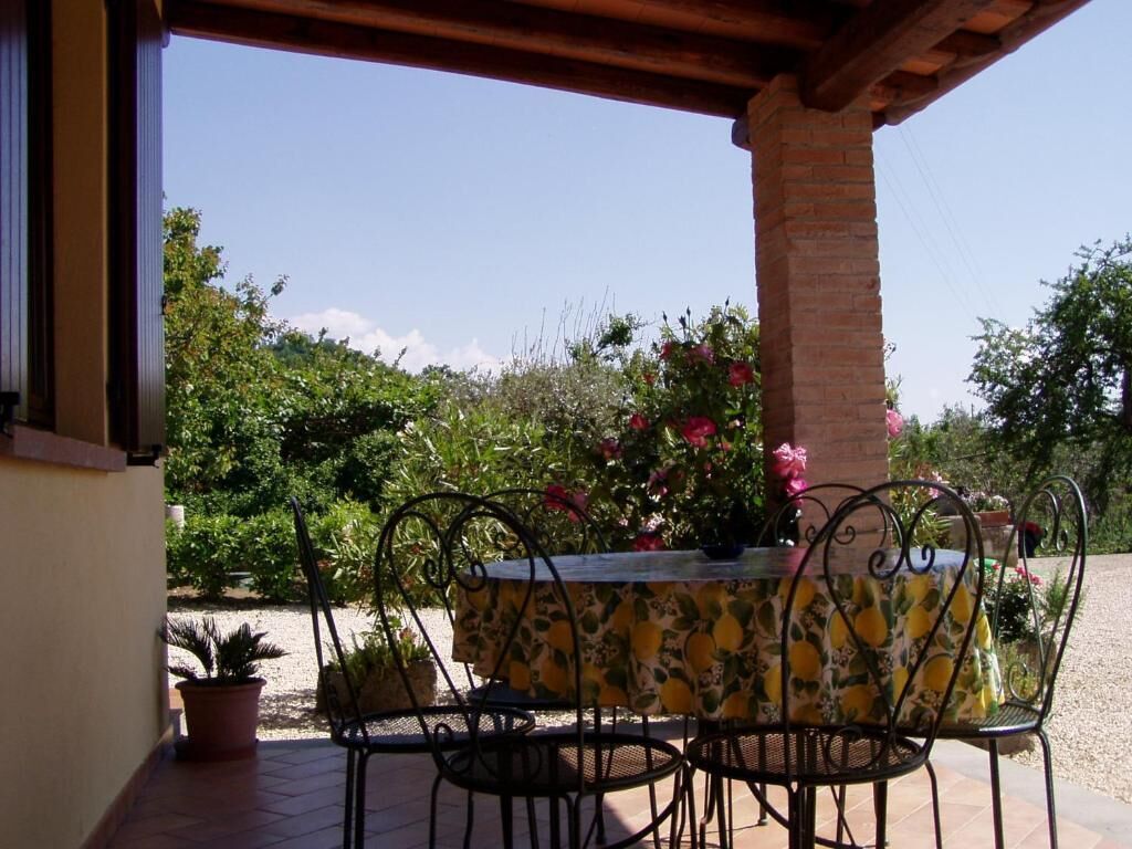 Un patio al aire libre con una mesa y sillas, rodeado de plantas en macetas y un pilar de ladrillo.
