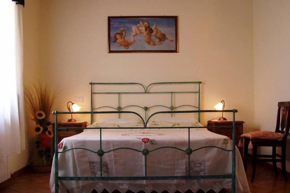 A room with a bed, two bedside tables, a chair, a lamp, and a painting on the wall.
