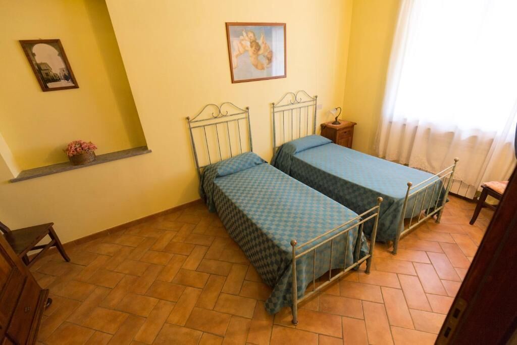 A room with two metal beds, a small wooden nightstand, a chair, and a shelf with a plant.