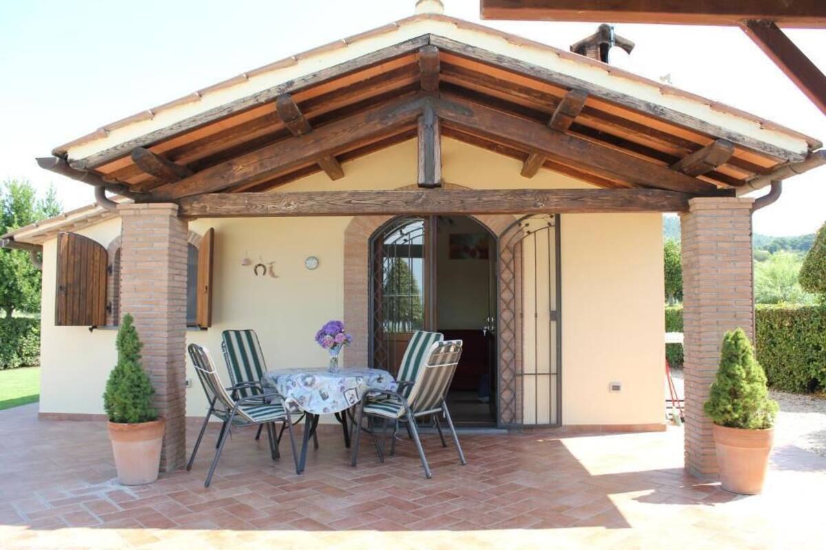 A covered patio with a table and chairs, a brick pillar, and a door leading inside.