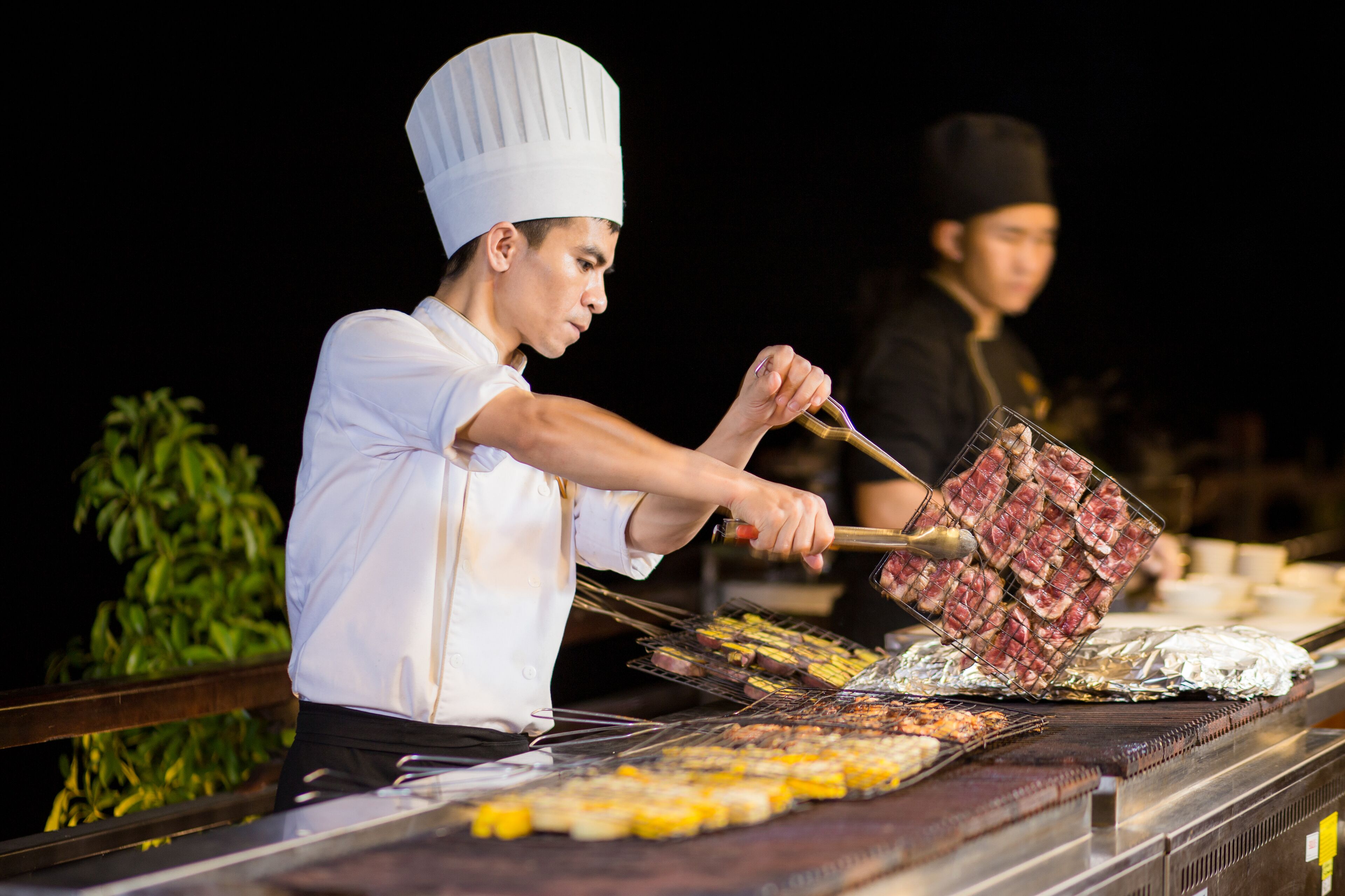 A chef grilling meat on a barbecue at night.