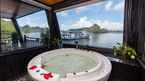 Une grande baignoire remplie de pétales de roses, un plafond en bois et une vue sur un bateau sur l’eau.