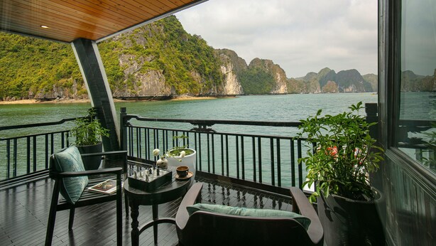 Une terrasse offrant une vue sur une baie et des falaises, aménagée avec des espaces pour s’asseoir à l’extérieur et des plantes en pot.