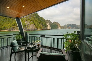 A deck with a view of a bay and cliffs, featuring outdoor seating and potted plants. - La Regina Grand Cruise (Tuan Chau)