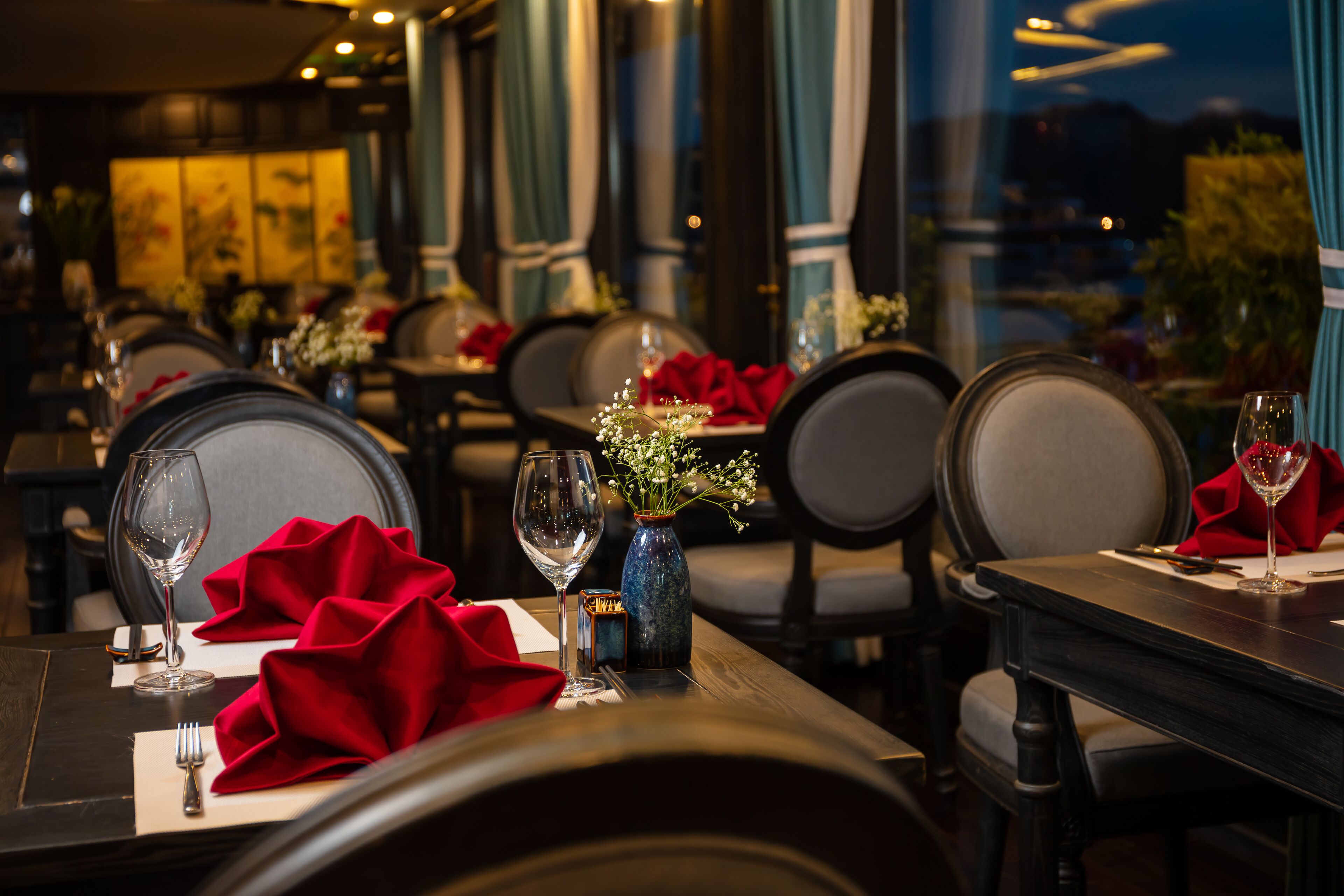 A restaurant with tables set for dining, featuring red napkins and glassware.