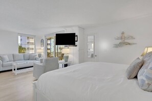 A hotel room with a large bed, a sofa, a chair, a television, and a balcony with a view of buildings. - 3RD FLOOR STUDIO | POOL-VIEW LANAI | KING BED | FREE PARKING | STEPS TO BONITA BEACH (Bonita Springs)