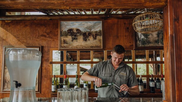 Una zona de bar con dispensador de agua, vasos y botellas de vino.