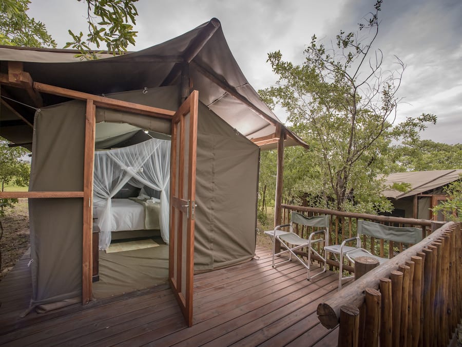 A tented accommodation with a wooden deck, a bed with mosquito netting, and a view of the surrounding trees.
