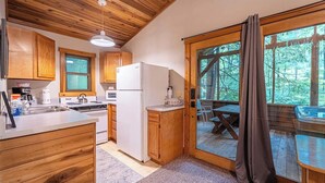 A kitchen with wooden cabinets, a refrigerator, a stove, and a sink. There is a large window with a view of trees.