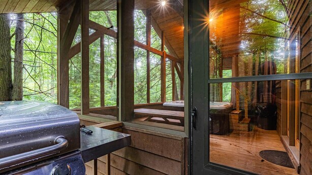 A rustic cabin with a wooden interior, a grill, and a view of the forest through large windows.