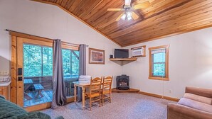 A cozy cabin interior with a wooden ceiling, a dining table with chairs, a fireplace, and a television.