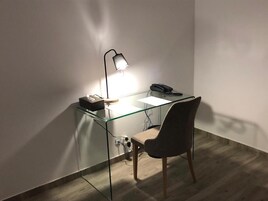 Uma mesa de escritório moderna com tampo de vidro, uma cadeira, uma luminária e um telefone.