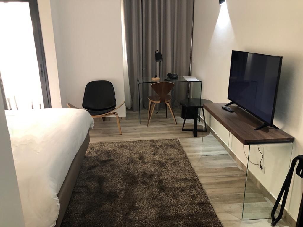 Habitación de hotel con cama, escritorio, computadora y silla, televisor y alfombra.