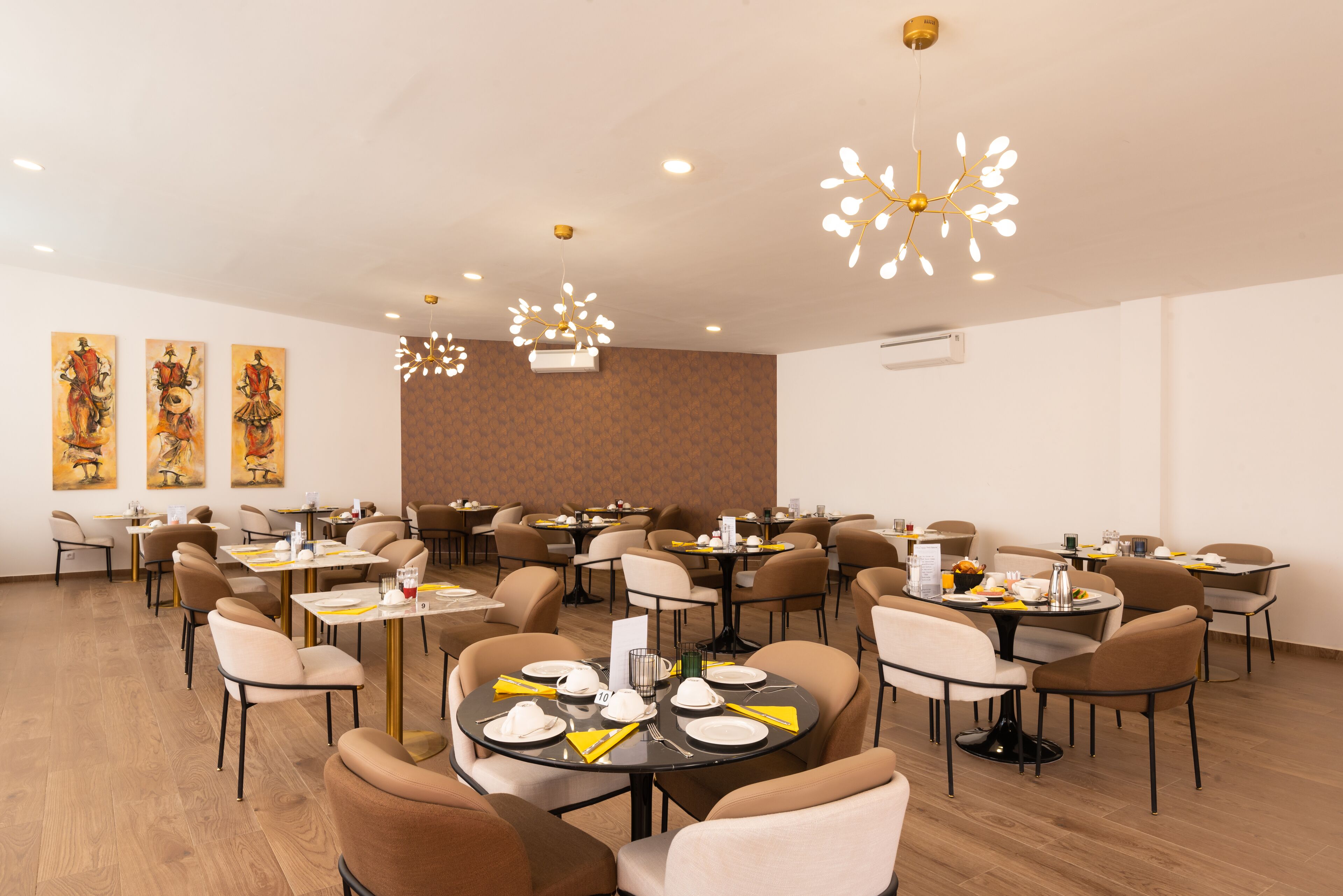 Un comedor espacioso con varias mesas redondas, sillas e iluminación moderna.