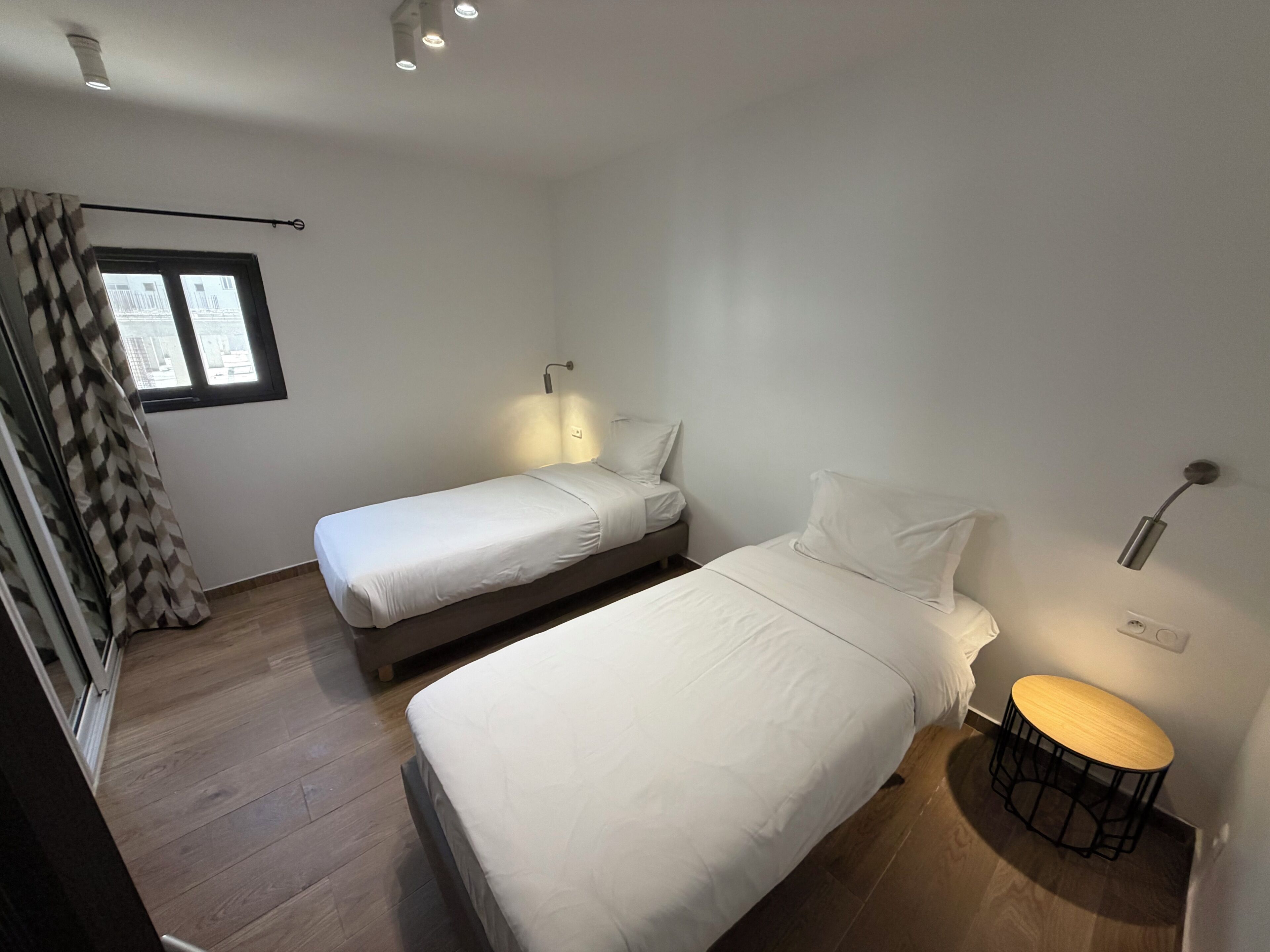 Une chambre avec deux lits, une fenêtre, une table de chevet et une petite table ronde.