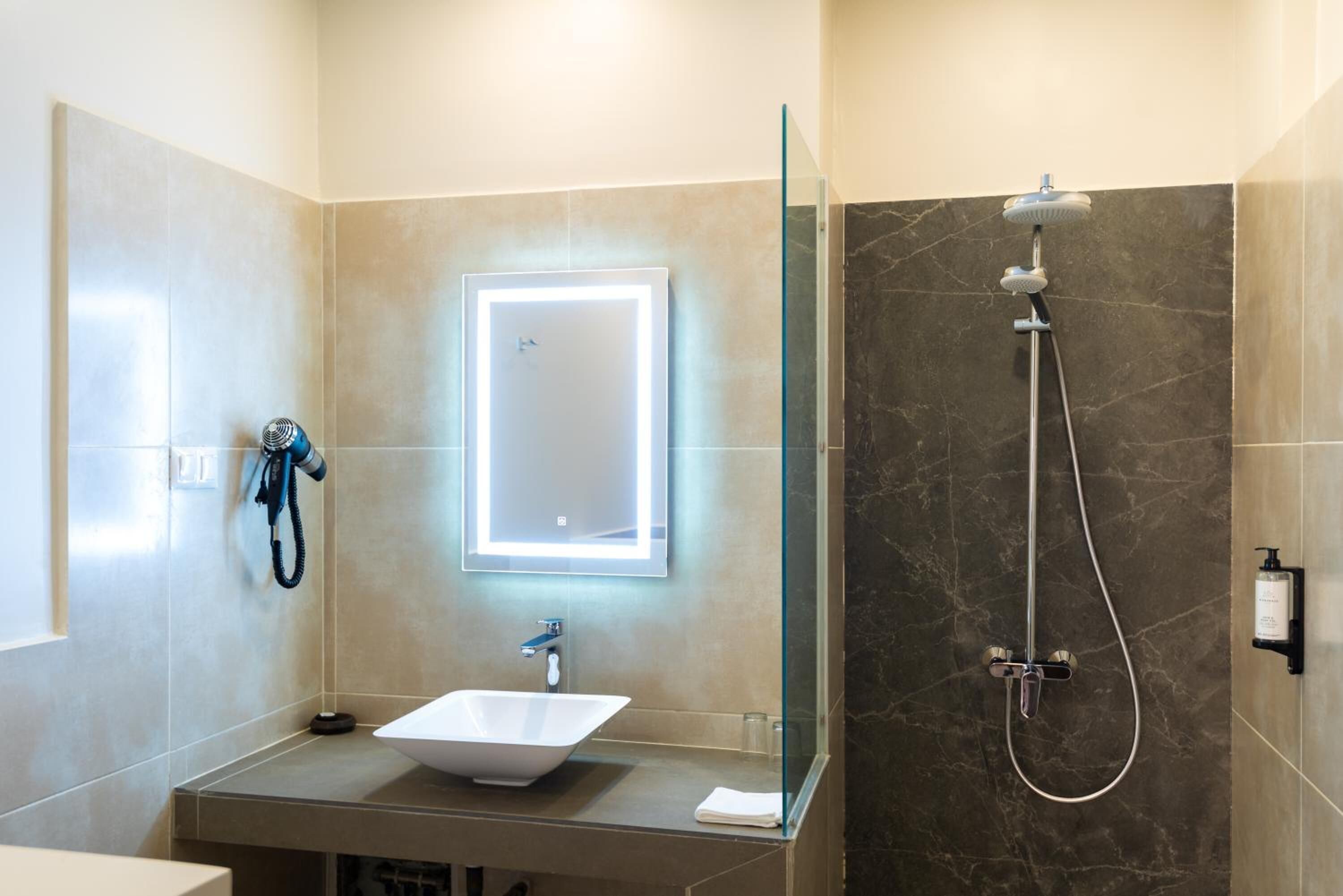 Ein modernes Badezimmer mit einer begehbaren Glasdusche, einem weißen Waschbecken und einem Spiegel mit integrierter Beleuchtung.