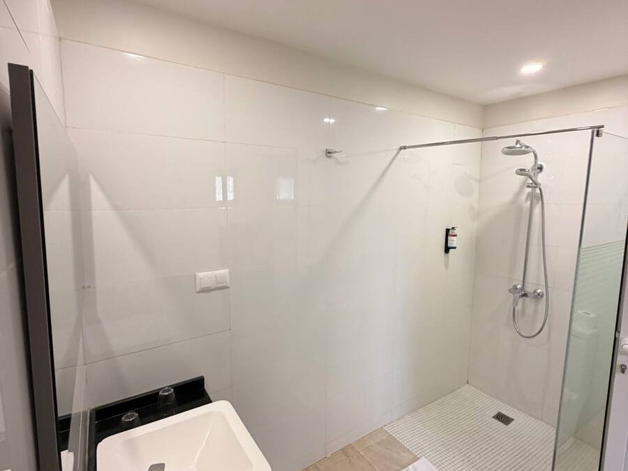 Un baño moderno con ducha de vidrio, un lavamanos blanco y un espejo.