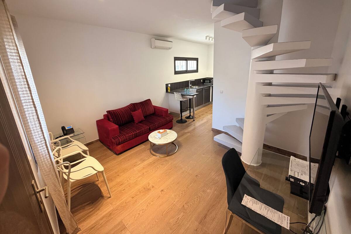 Una sala de estar moderna con un sofá rojo, una mesita redonda, una zona de cocina con microondas y un diseño de escalera único.