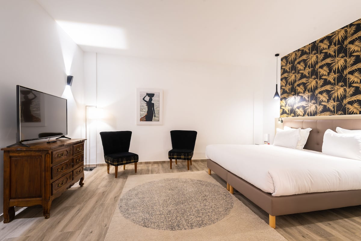 Un dormitorio con una cama, un aparador, dos sillas, un televisor y un muro con estampado tropical.