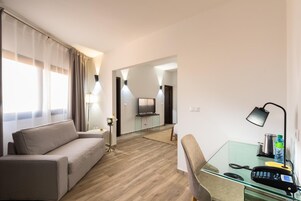 Una habitación de hotel moderna con un sofá, un escritorio de vidrio con un teléfono, una lámpara y un televisor al fondo.
