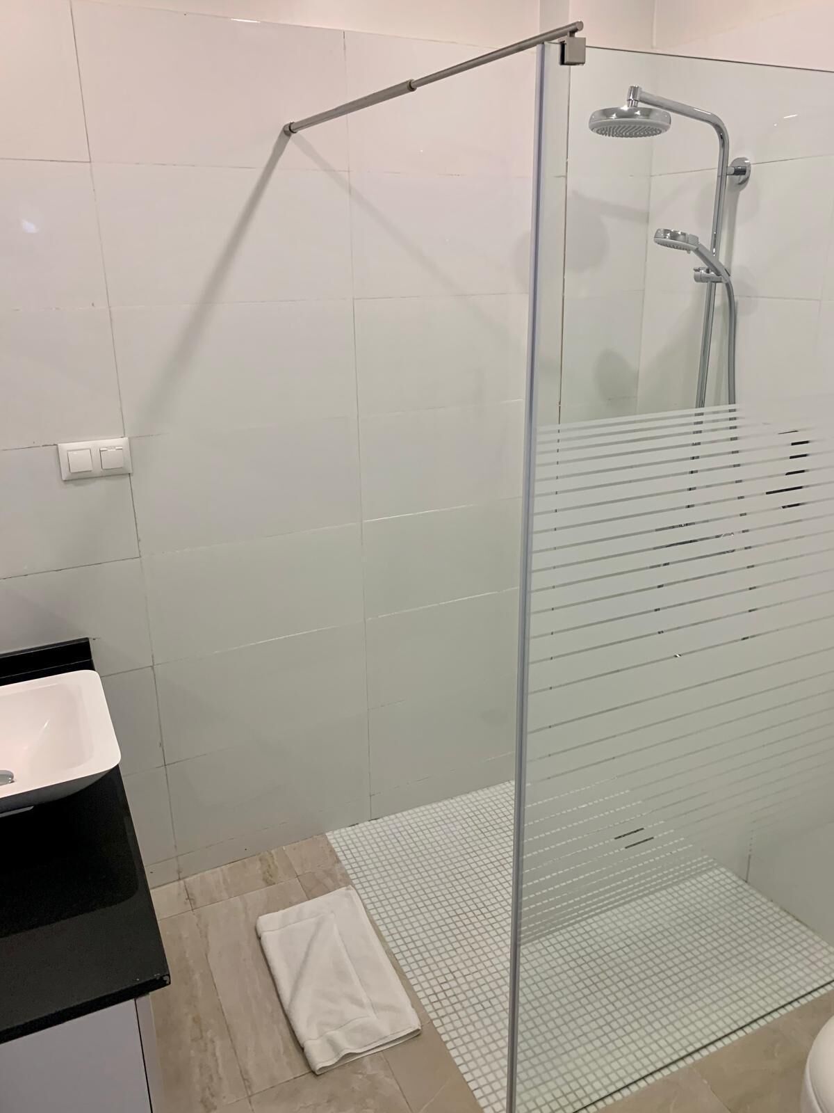 Un bagno moderno con doccia vetrata, lavandino bianco e pavimento piastrellato.