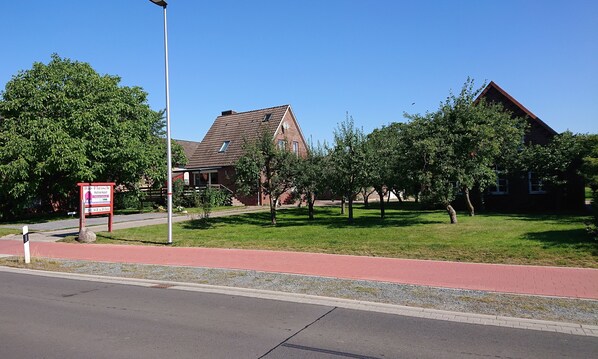 A building with a sloped roof, a paved walkway, and a grassy area with trees.