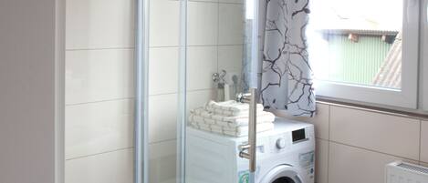 Een moderne badkamer met een douchecabine van glas, een wasmachine en een raam met uitzicht op een gebouw.