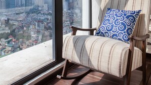 Una habitació amb un gran finestral que ofereix vista a la ciutat, un butac armchair amb coixí estampat i un paviment de fusta.