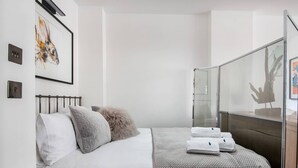 Una camera da letto moderna con un letto, cuscini, box doccia in vetro e un quadro appeso al muro.
