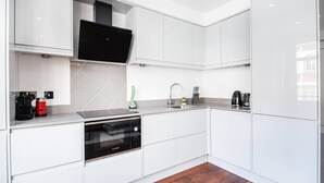 Eine moderne Küche mit weißen Schränken, einem Geschirrspüler von Bosch, einem eingebauten Backofen, einer Kaffeemaschine und einem Wasserkocher.