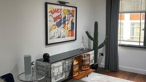 Un soggiorno moderno con un divano blu, un tavolino in vetro, un mobile decorativo, un cactus e un'ampia finestra con tende.