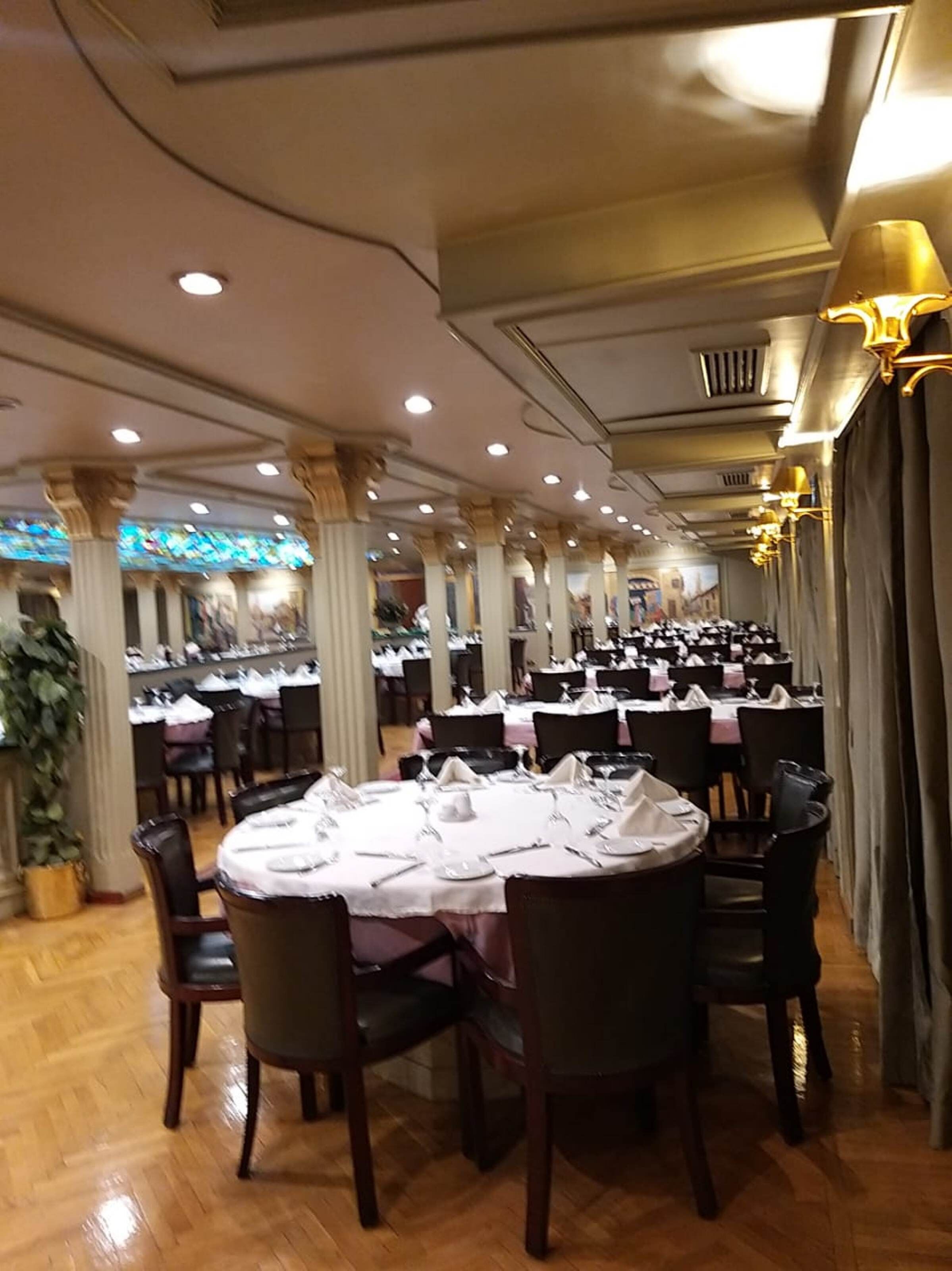 A banquet hall with round tables set for dining, featuring a classic design with wooden chairs and white tablecloths.