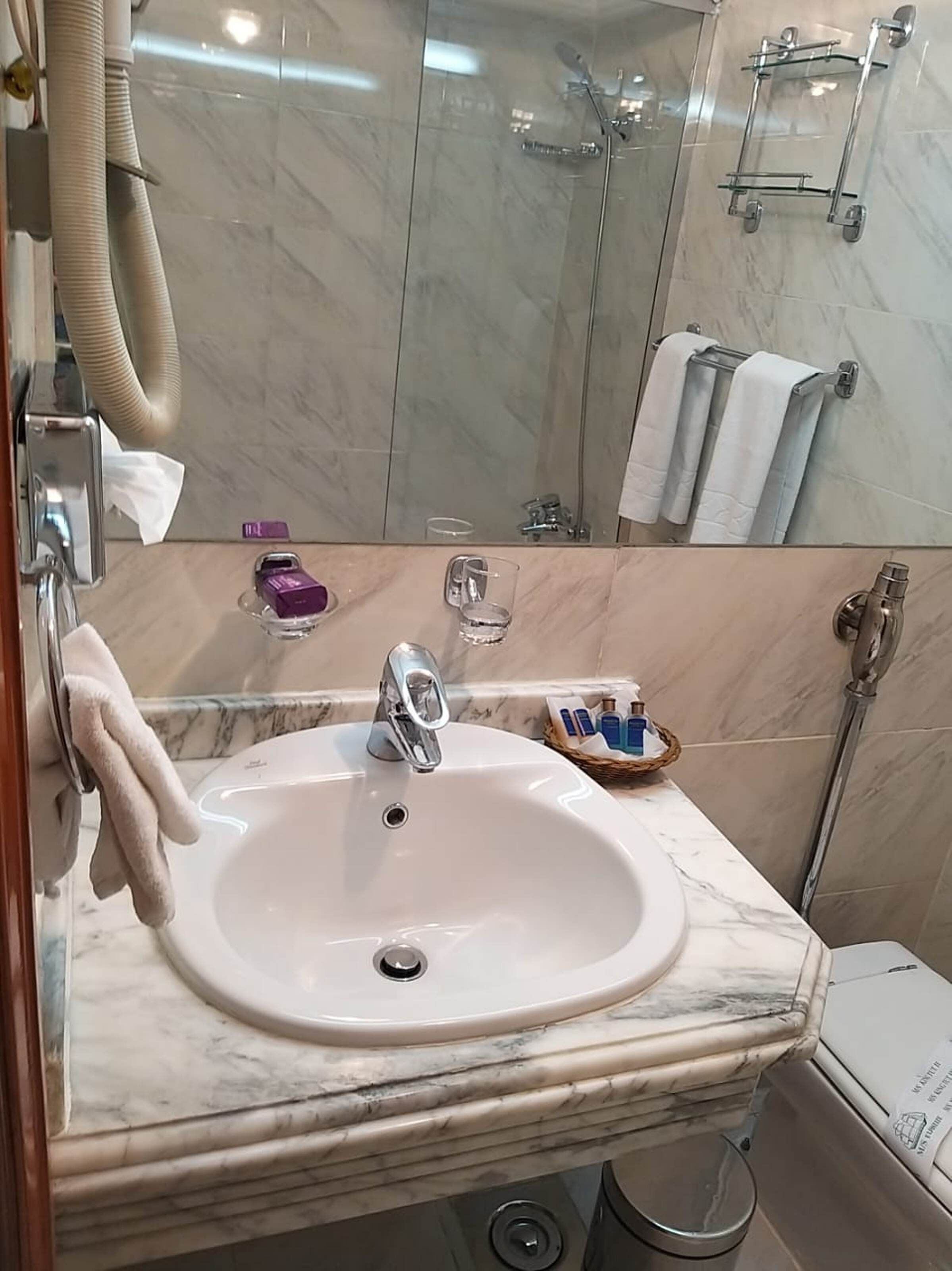 A bathroom with a marble sink, a handheld showerhead, and a glass-enclosed shower.