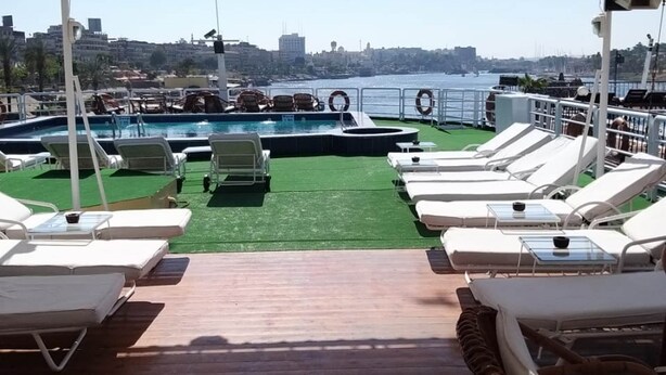 A covered deck with a pool, lounge chairs, and a view of the city skyline. - MS King Tut I Nile Cruise (Luxor)