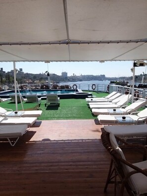 Um deck coberto com piscina, cadeiras de lounge e vista para o horizonte da cidade.