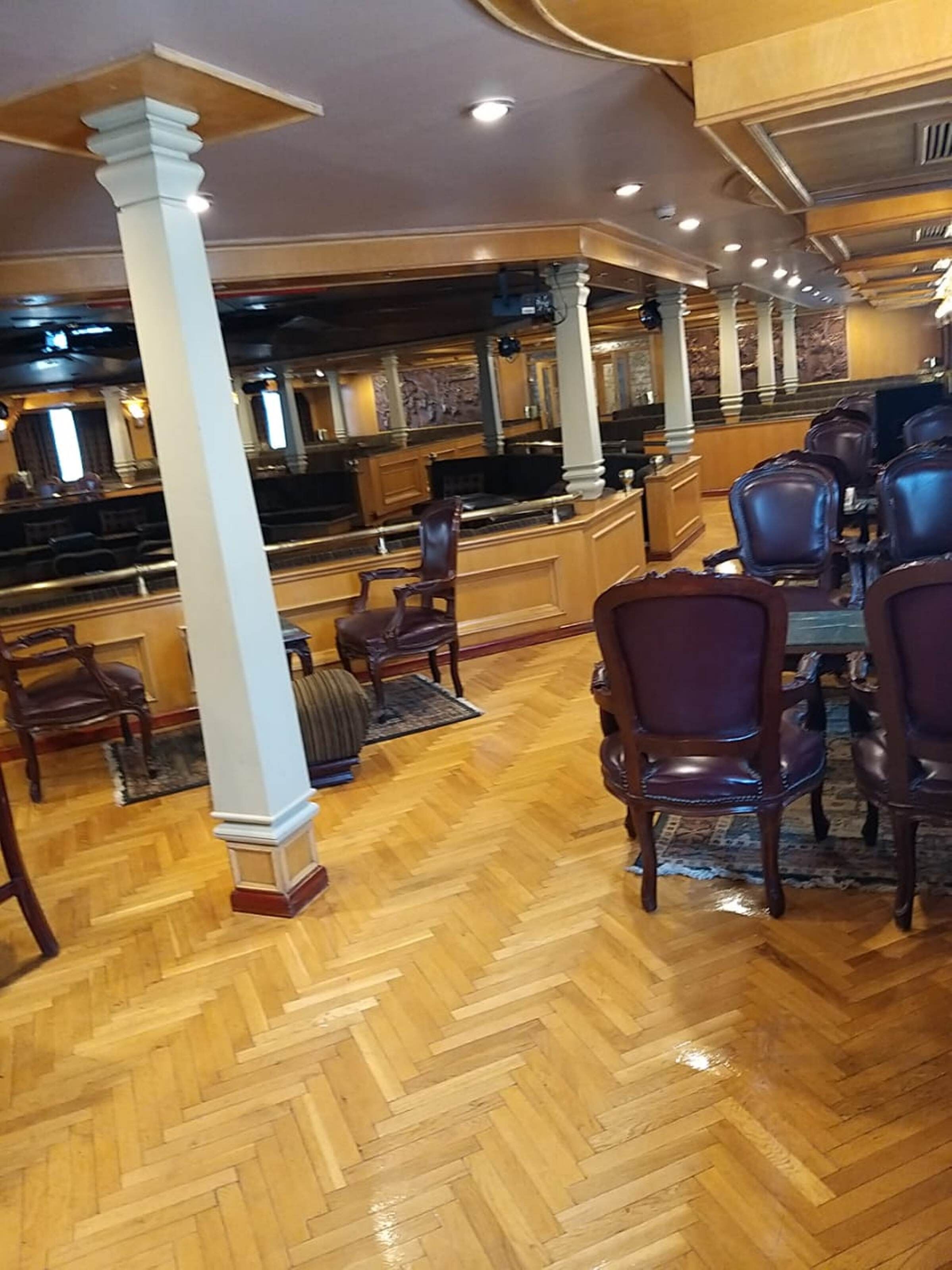 Un restaurante con suelo de madera, una zona de bar y varias sillas de color oscuro.