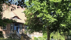 Ein Gebäude aus Ziegelsteinen mit rotem Ziegeldach, einer Treppe zum Eingang und einem Baum davor.
