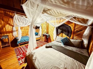 A room with a bed under a canopy, wooden walls, and a patterned rug. - The Little H'mong House (Ta Van)