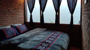 A rustic room with a brick wall, a wooden ceiling, and a bed with patterned bedding. - The Little H'mong House (Ta Van)