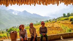 Three individuals seated on a bench with a mountainous landscape in the background. - The Little H'mong House (Ta Van)