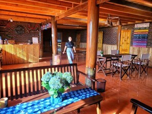 A wooden interior with a reception desk, a bench with a vase of flowers, and a table with chairs. - The Little H'mong House (Ta Van)