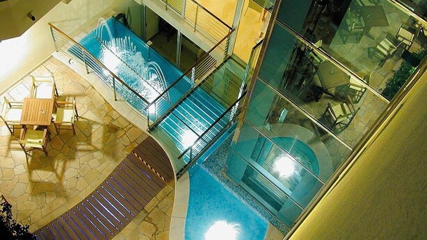 A modern indoor pool area with glass railings, a seating area, and a staircase leading to upper levels. - Hotel Albatros (Misano Adriatico)