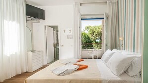 A hotel room with a bed, a TV, a bathroom, and a balcony with a view of trees. - Hotel Albatros (Misano Adriatico)