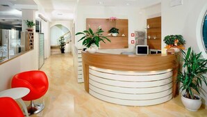 A modern reception area with a curved reception desk, red chairs, and potted plants. - Hotel Albatros (Misano Adriatico)