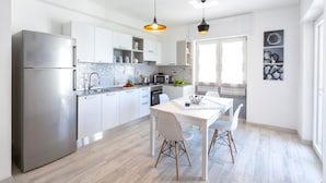 Una cocina moderna con armarios blancos, electrodomésticos de acero inoxidable y un comedor con mesa y sillas blancas.