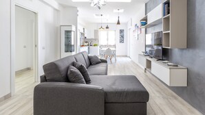 Una sala de estar moderna con un sofá seccional gris, un mueble empotrado para televisión y un comedor al fondo.